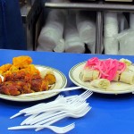 A blue counter with two plates on top of it, one with bananas and onions and another with sausages and alcapurrias.