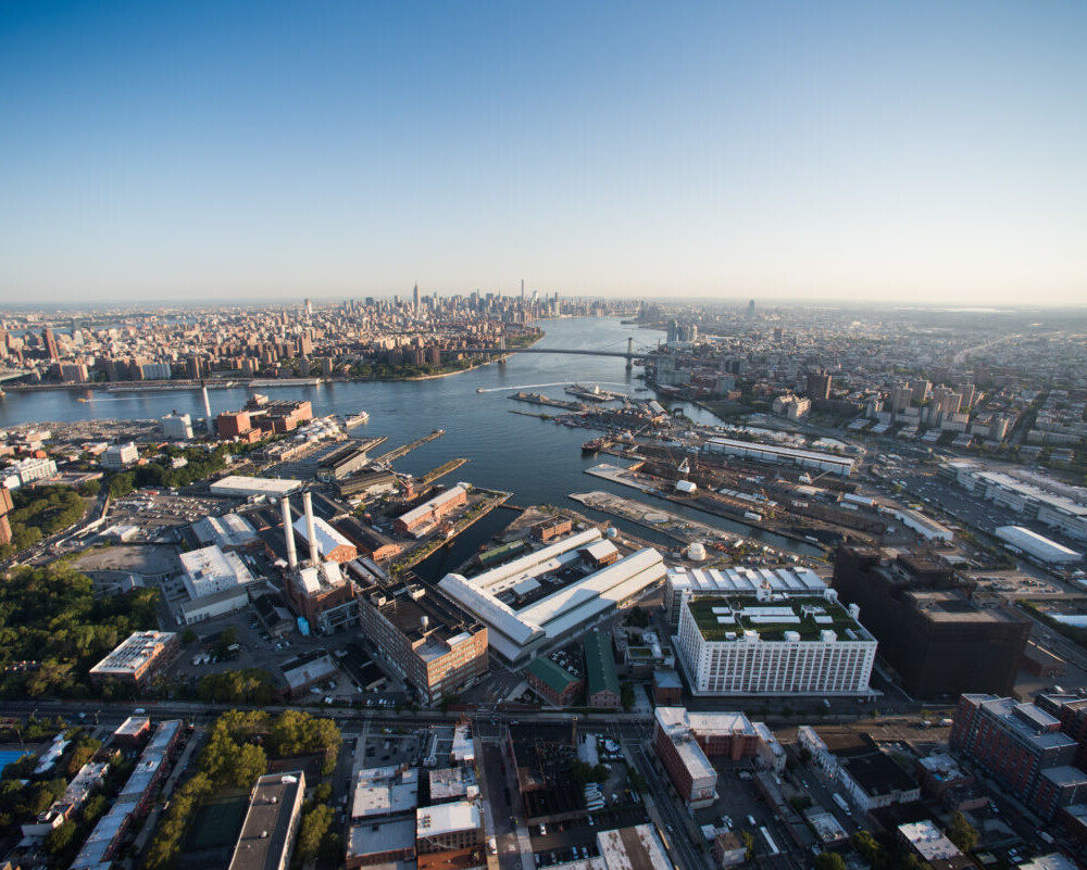 Aerial view that shows the Brooklyn Navy Yard with Wallabout Bay, the East River, and the Manhattan and Williamsburg Bridges and Manhattan in the background