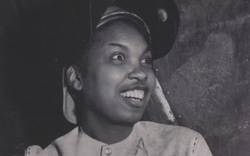 An African-American female wearing a welder's helmet flipped up. She is smiling and looks surprised.