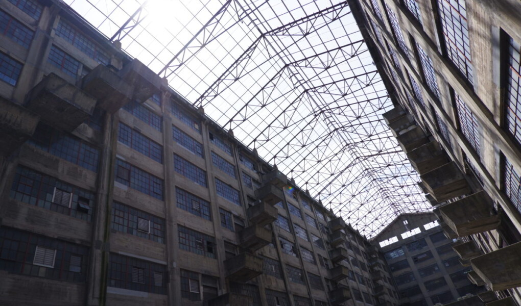 View of the metal frames that span the two sides of Building B, a massive concrete industrial building with an atrium at the center that opens to the sky.
