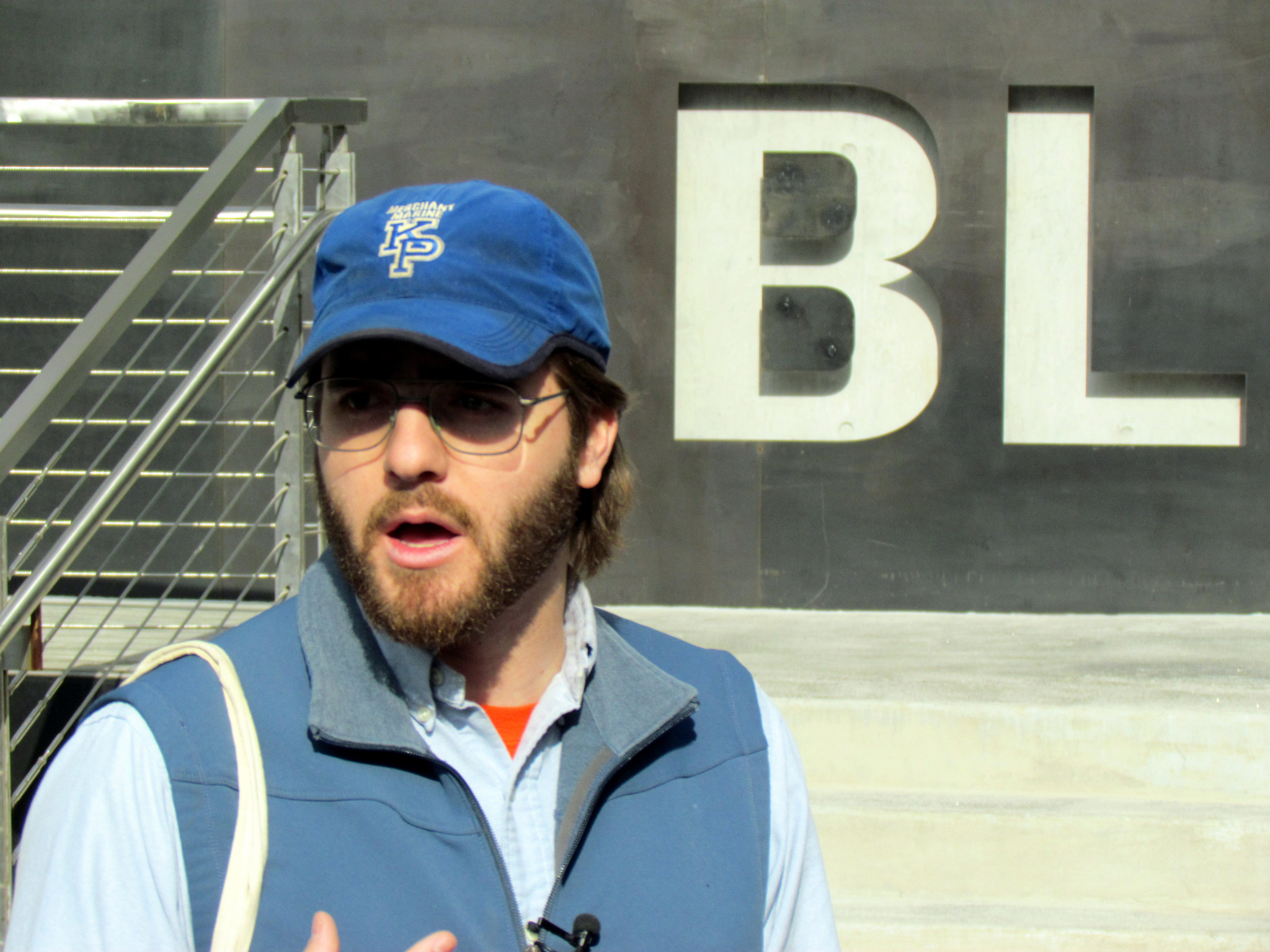 Andrew Gustafson standing outside in front of BLDG 92 museum wearing a hat reading "KP" for Kings Point