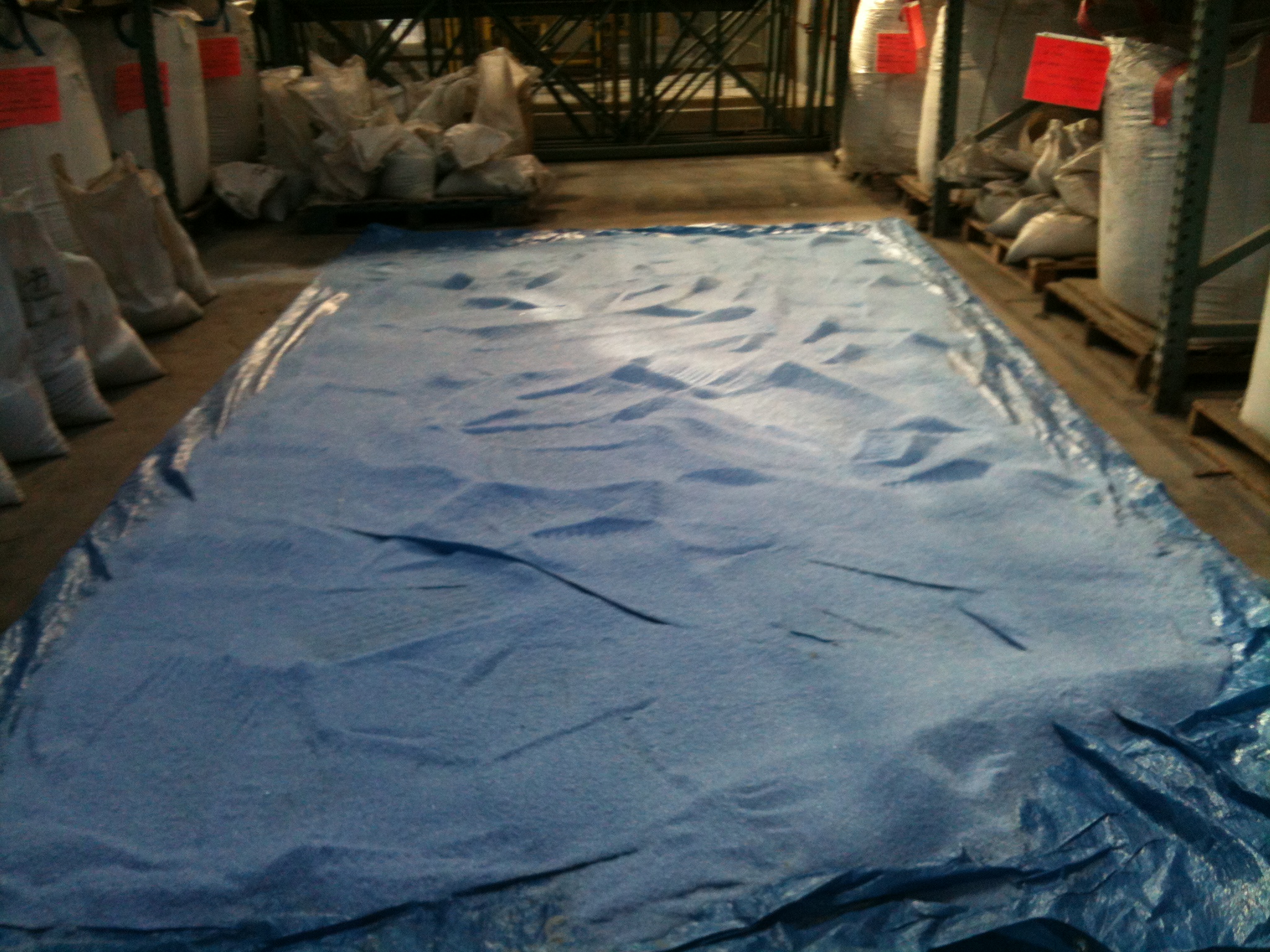 A tarp laid out on the factory floor with blue fine glass shards spread out.