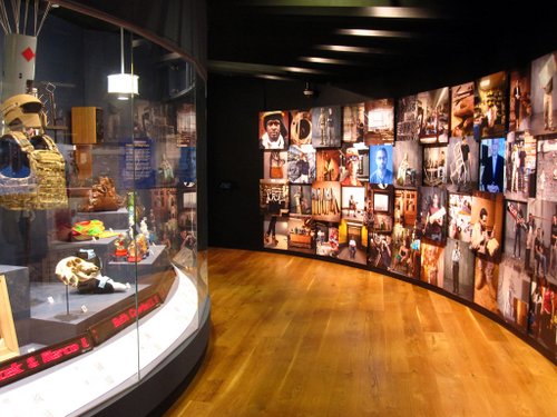 A museum exhibit that includes a series of photographs and videos to the right and an exhibit case with commercial products to the left