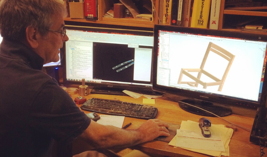 Sitting at his desk using a mouse and looking at a screen with a chair on it, Scott Jordan builds a chair, virtually.