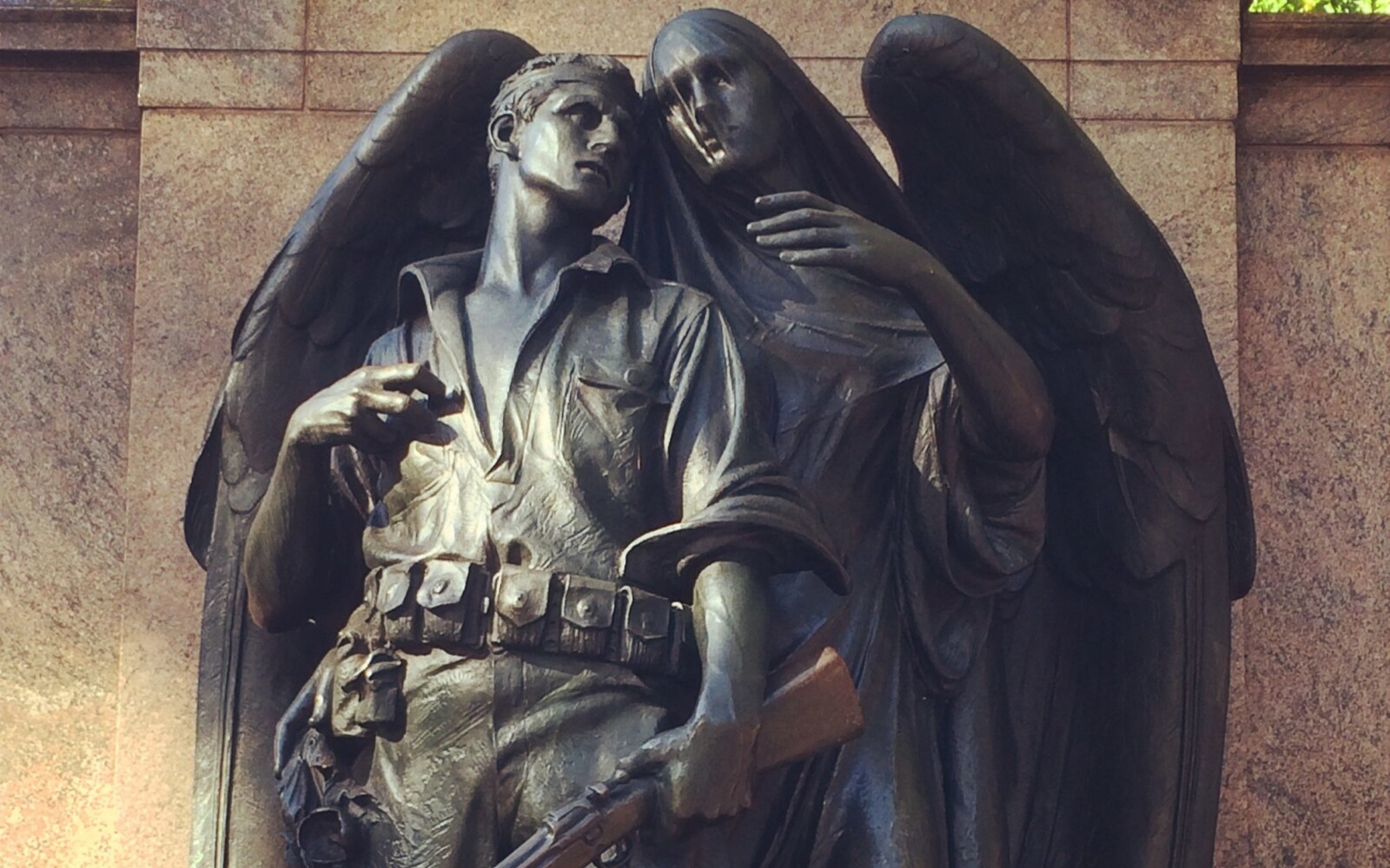 A statue of a soldier who stands clutching his gun and looking off into the distance as an angel begins to wrap her wing and arm around him