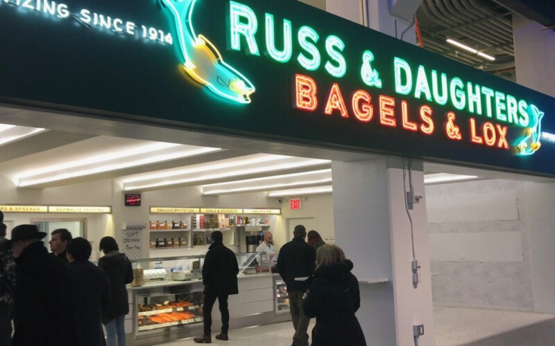 A bright but old-fashioned looking neon sign at a retail shop that has a fish graphics and reads Russ and Daughters Bagels and Lox appetizing since 1914