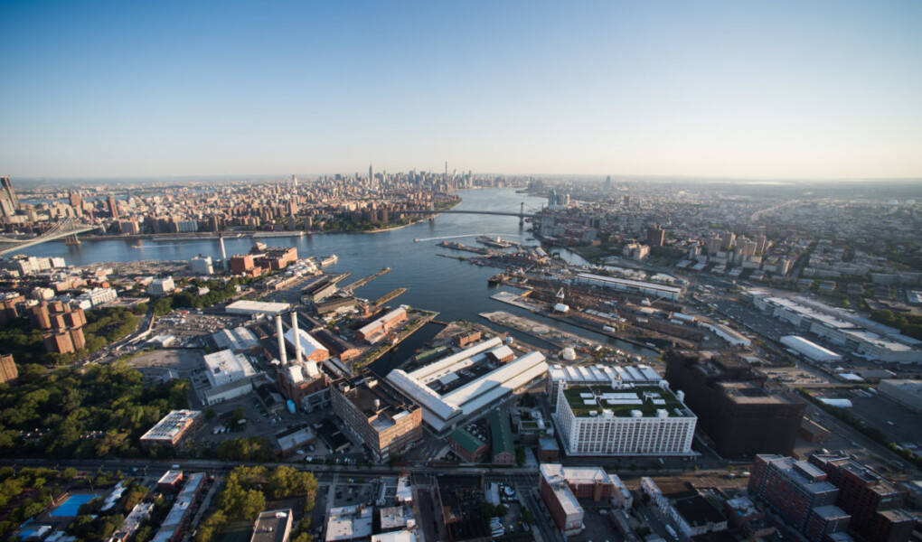 Aerial view that shows the Brooklyn Navy Yard with Wallabout Bay, the East River, and the Manhattan and Williamsburg Bridges and Manhattan in the background