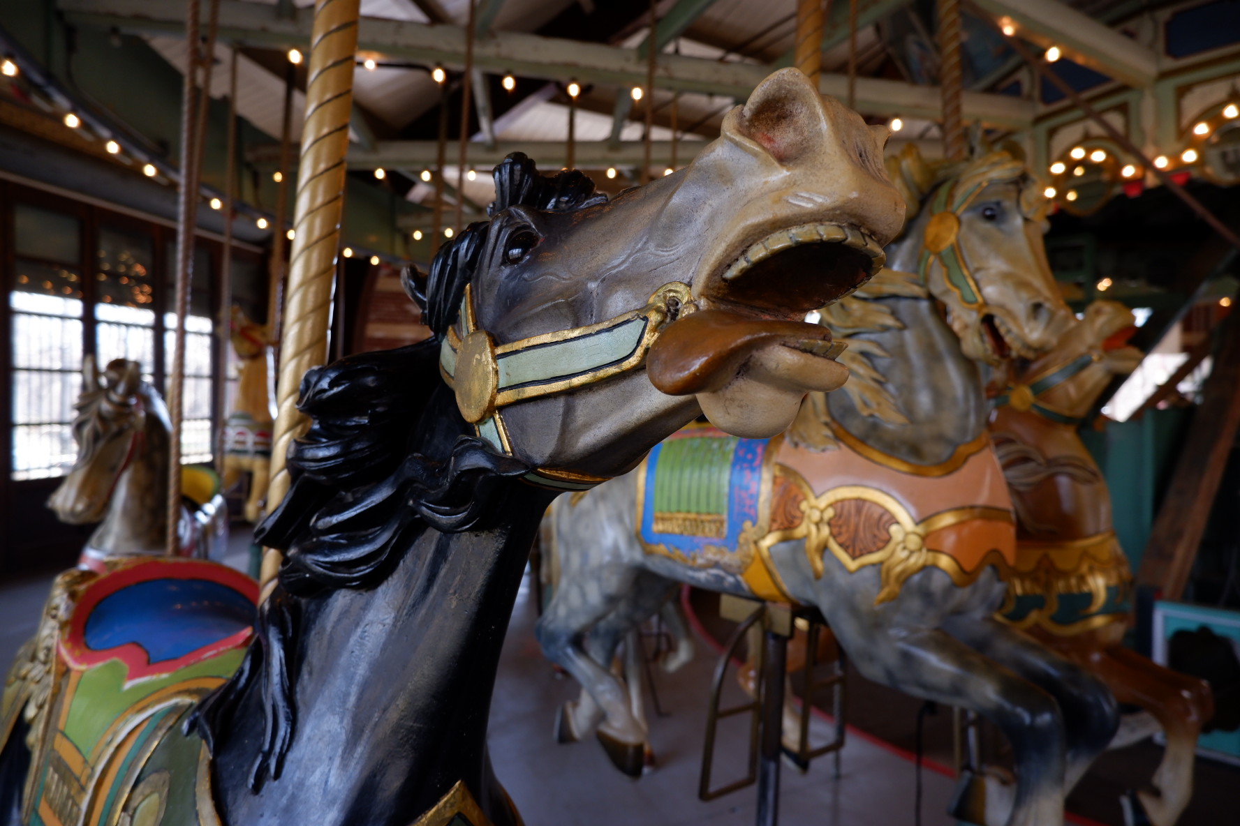 A close-up of a carved black stallion with lolling tongue and wind-blown mane at the Prospect Park Carousel