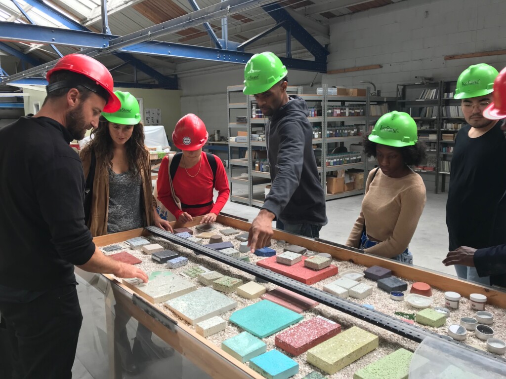 A tour at IceStone with 7 people looking at and handling samples of counter tops in a factory space