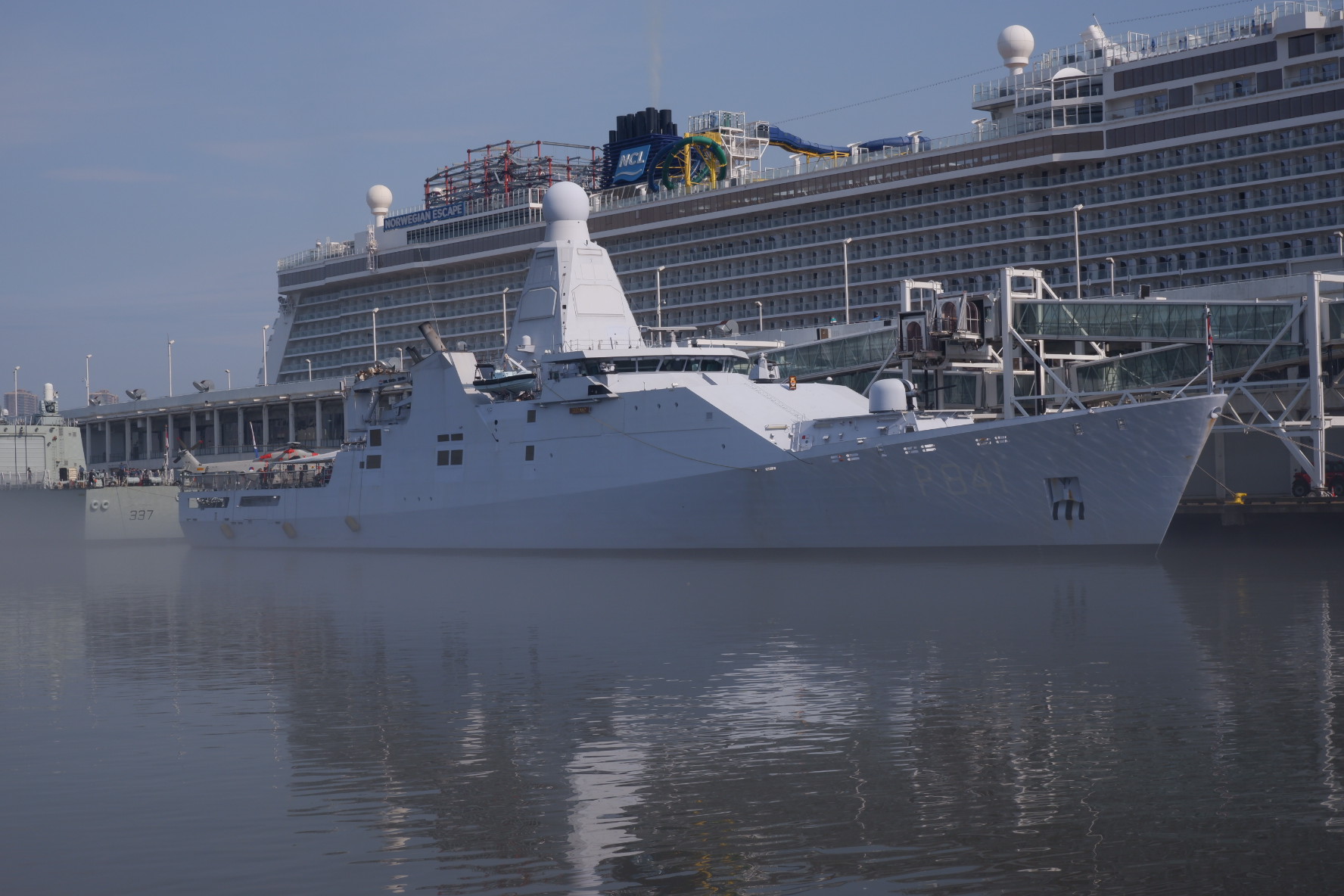 A white off-shore patrol vessel of the Royal Netherlands Navy moored at a pier with a cruise ship in the background