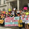 Street vendors rally on the steps of city hall with signs that read I love immigrant NY and Support NYC smallest businesses and Help us to serve you