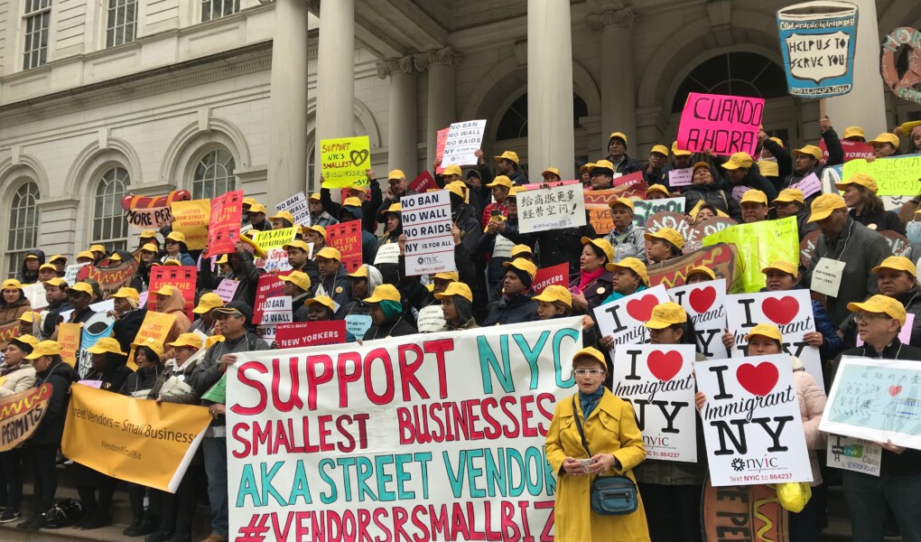 Street vendors rally on the steps of city hall with signs that read I love immigrant NY and Support NYC smallest businesses and Help us to serve you