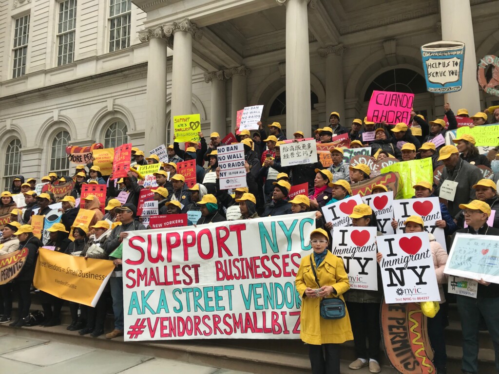 Street vendors rally on the steps of city hall with signs that read I love immigrant NY and Support NYC smallest businesses and Help us to serve you