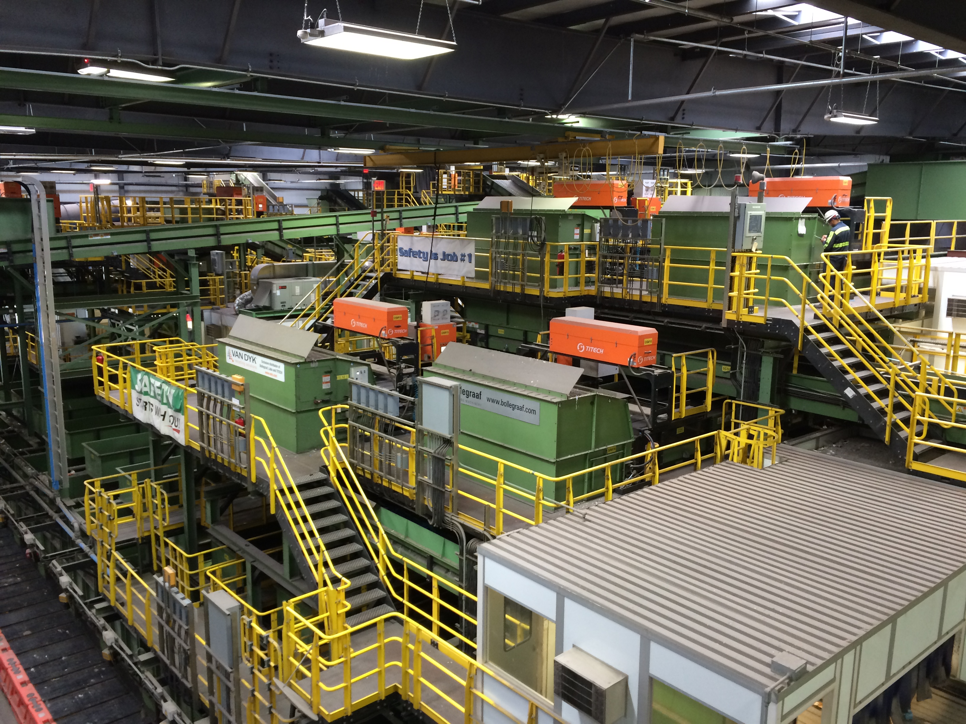 Inside recycling facility showing green machinery on multiple levels inside a large warehouse building.
