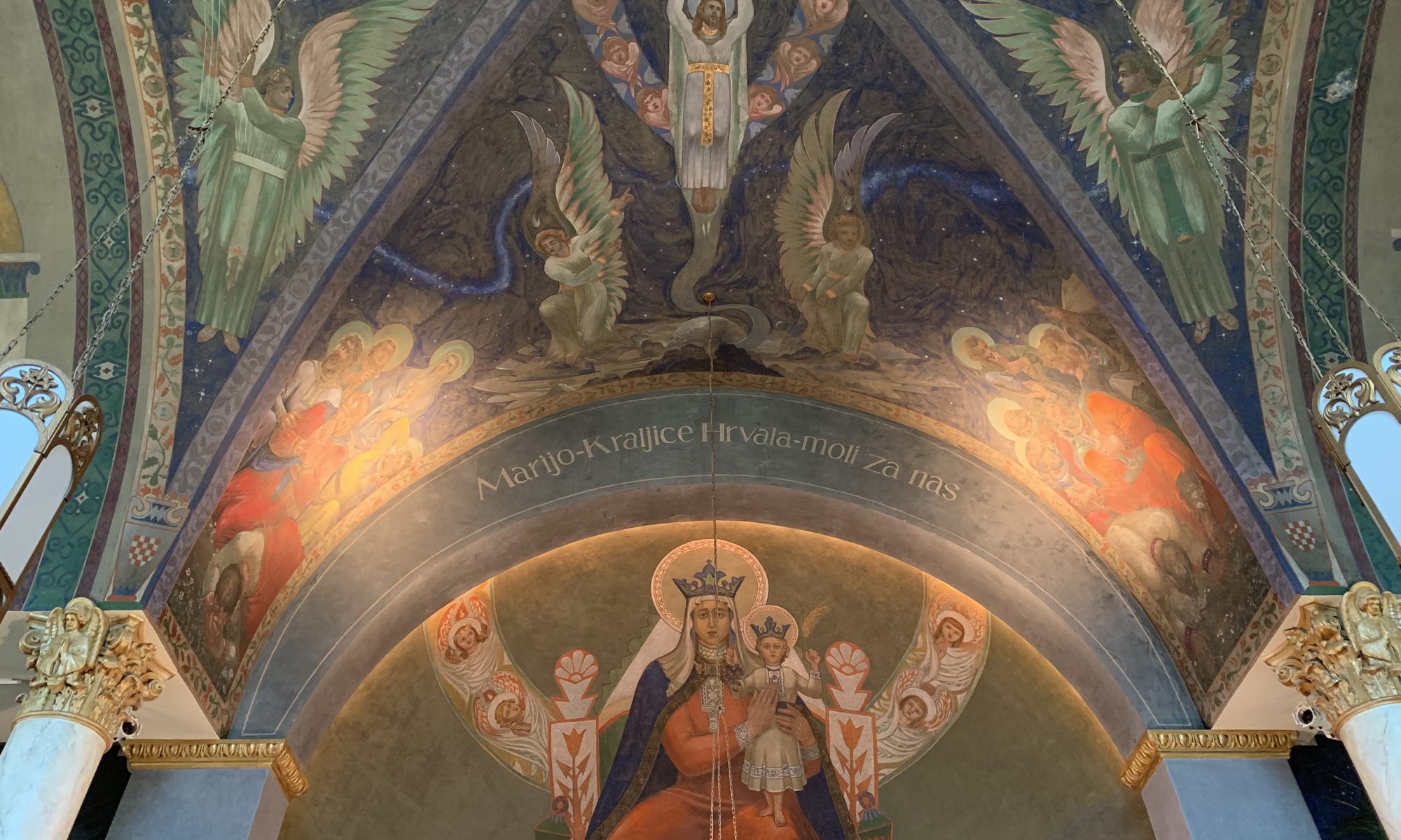 Photo of a church ceiling painted by artist Maxo Vanka depicting Mother Mary wearing a red robe and Baby Jesus on her lap, Jesus ascending to heaven above her