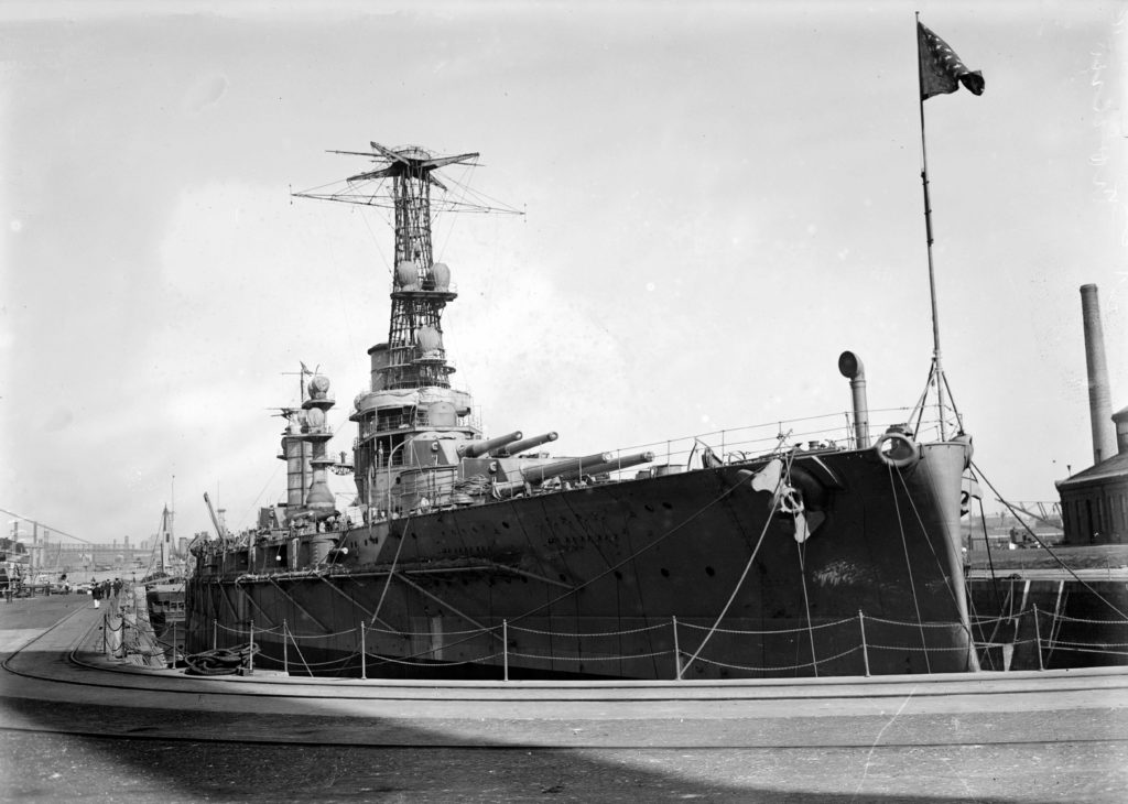 Black and white photo of a battleship in dry dock with the bow facing the camera