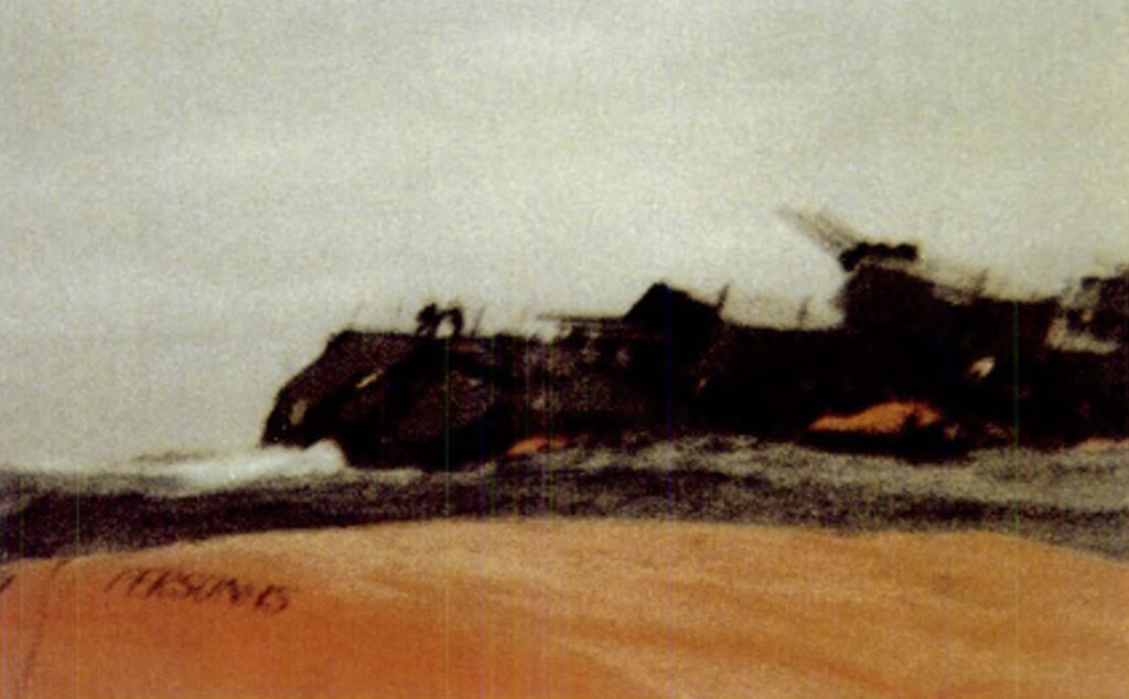Color photo of the Belgrano sinking, with outlines of two figures standing on the bow visible.