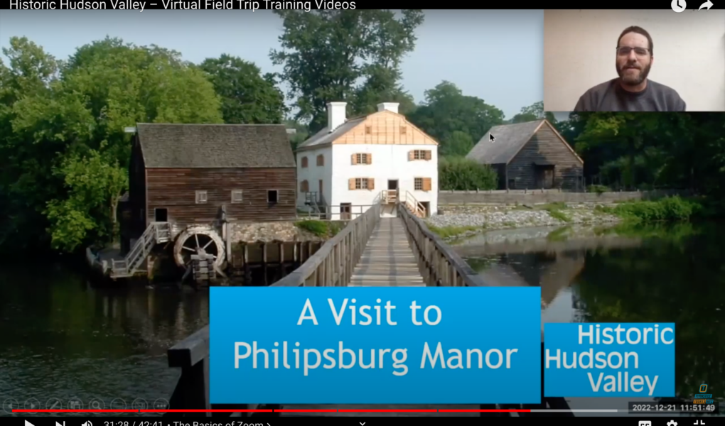 A man in a beard and classes appears in a box in the upper right-hand corner while the rest of the screen is taken up with an image of a white historic house with a bridge in the foreground and text that reads a visit to Philipsburg Manor